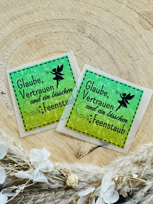 grün gelbes Bügellabel Etikett mit dem Spruch Glaube, vertrauen und ein bischen Feenstaub in schwarzer Schrift mit einer kleinen Zauberfee.