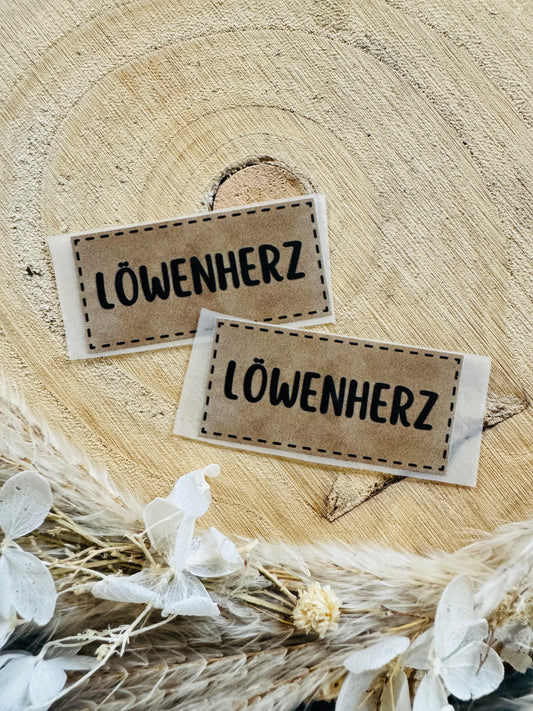 hellbraunes Bügellabel Etikett mit dem Spruch LÖWENHERZ in schwarzen Buchstaben