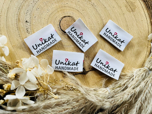 weisses Weblabel mit der Aufschrift Unikat Handmade in schwarzer Schrift mit einem kleinen roten herzchen