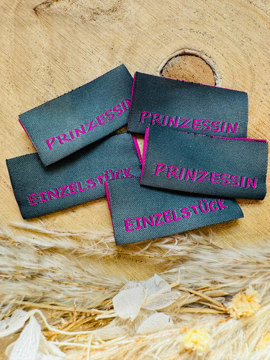 graues Weblabel mit der Aufschrift Prinzessin und Einzelstück auf jeweils einer Seite in rosa Schrift