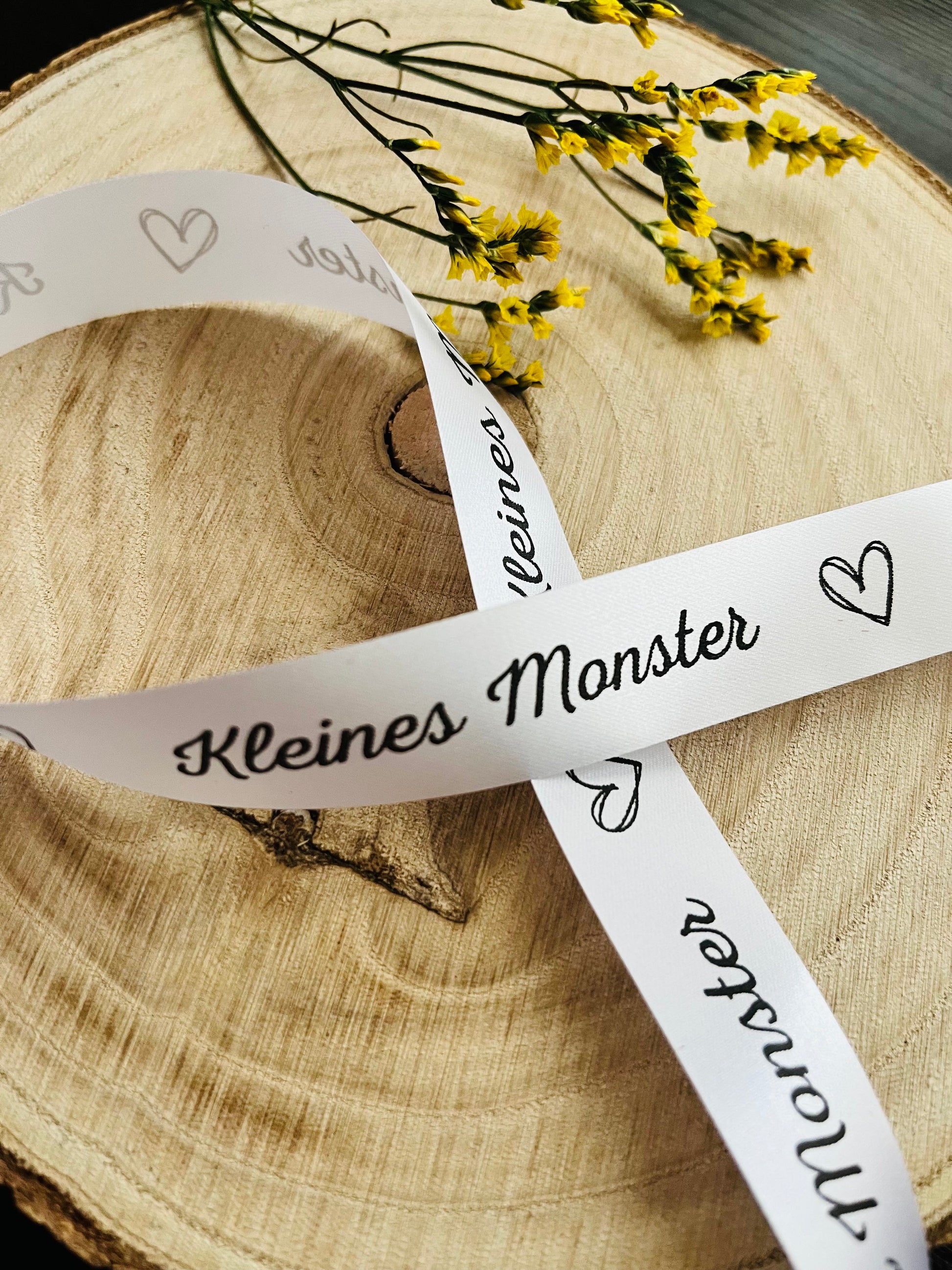 weisses Satinband mit dem fortlaufenden Spruch Kleines Monster und Herzchen, Breite zwei Zentimeter.