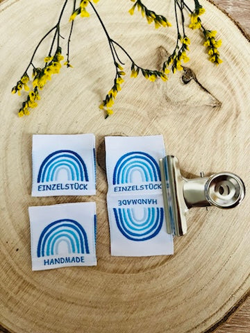 weisses Weblabel mit einem Regenbogen in blauen Farben und darunter das Wort Einzelstück und Handmade in blauer Schrift