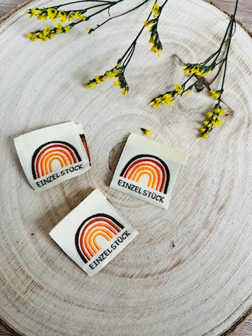 weisses Weblabel mit einem bunten regenbogen und darunter das Wort Einzelstück in schwarzer Farbe