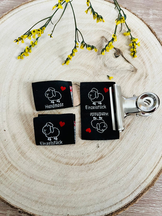 schwarzes Weblabel mit einem kleinen Schäfchen und dem Spruch Handmade und Einzelstück je auf einer Seite in weiss mit einem roten herzchen