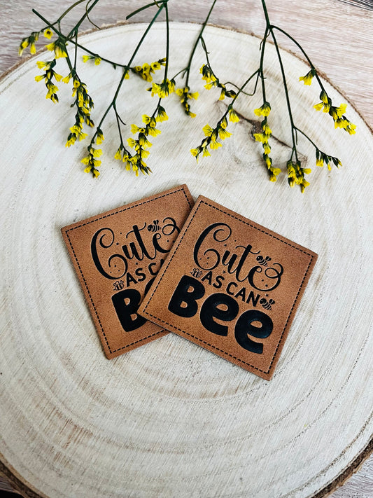 braunes kunstlederlabel mit dem spruch cute as can bee und kleinen bienchen abgebildet