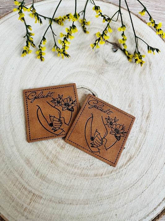 braunes kunstlederlabel mit dem spruch geliebt und einer kleinen kinderhand die die hand der mutter umfasst
