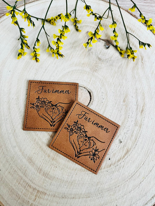 braunes kunstlederlabel mit dem spruch für immer und zwei händen die zwei kleine babyfüsschen zu einem herz geformt halten