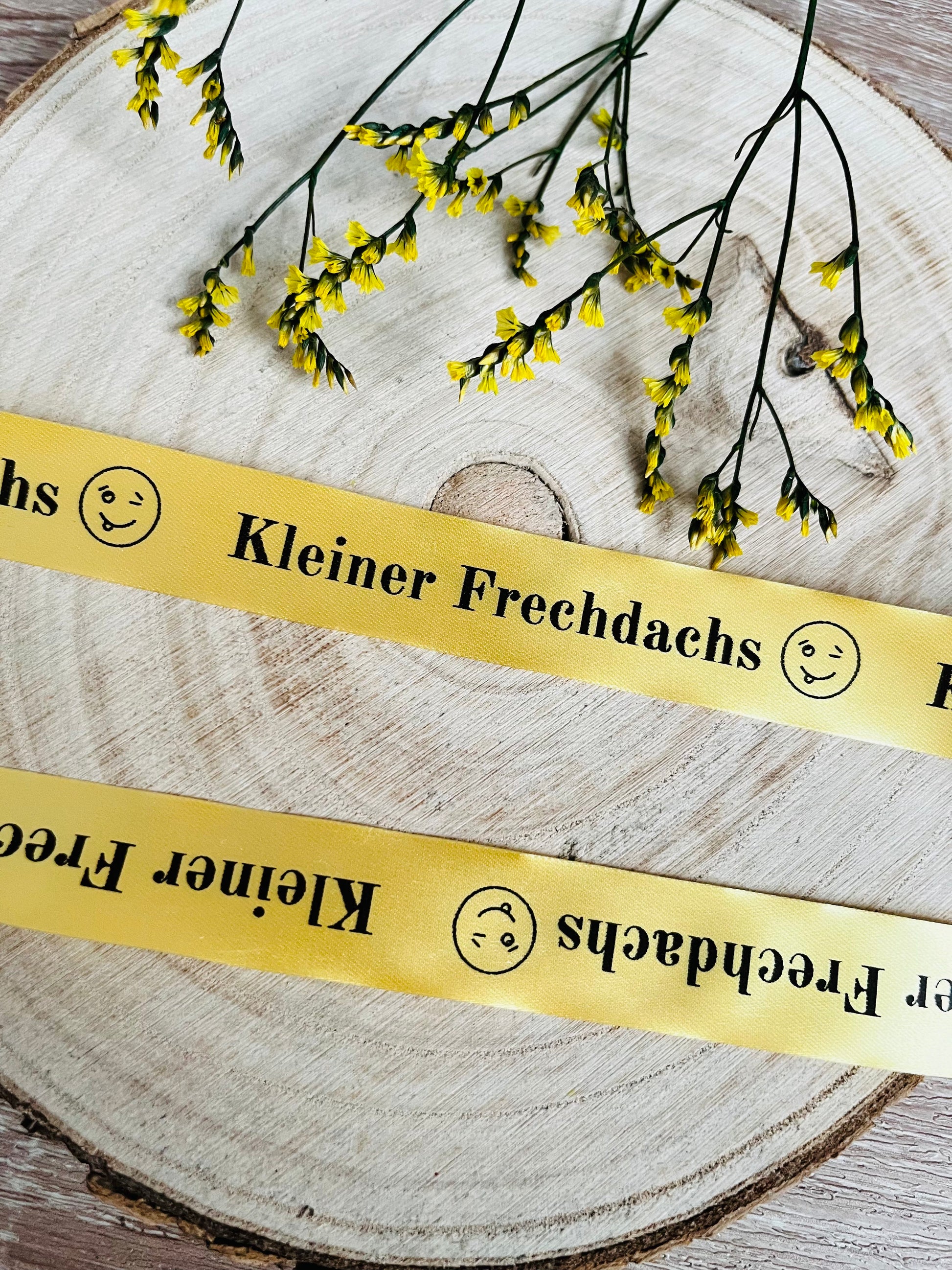 gelbes Satinband mit dem fortlaufenden Spruch Kleiner Frechdachs und einem Smiley, Breite zwei Zentimeter.