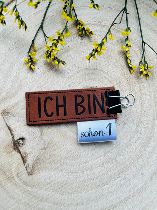 braunes Kunstlederlabel mit dem Spruch Ich bin und verschiedenen gewebten Labeln zum Beispiel Motiv schon Eins kombinierbar