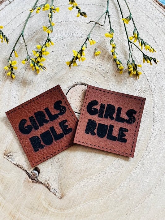 braunes Kunstlederlabel mit dem Spruch Girls Rule in schwarzen Buchstaben