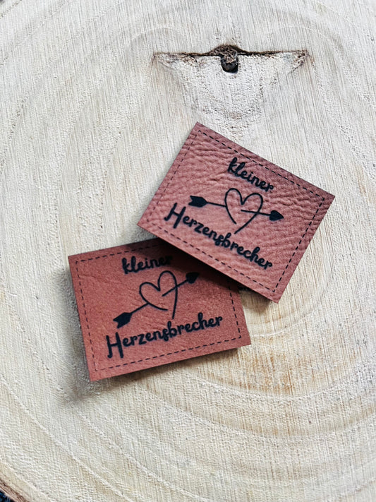 braunes Kunstlederlabel mit dem Spruch kleiner Herzensbrecheer und einem Herz mit Amor Pfeil
