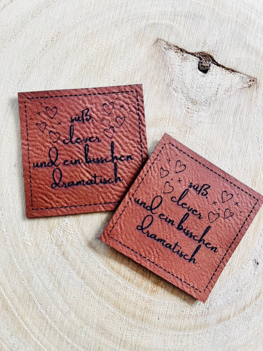 braunes Kunstlederlabel mit dem Spruch süß clever und ein bischen dramatisch mit kleinen Herzchen