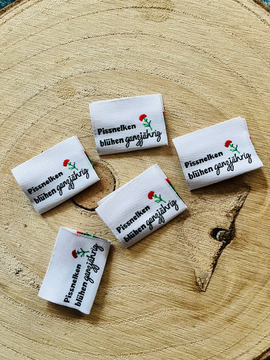 weisses Weblabel mit dem Spruch Pissnelken blühen ganzjährig in schwarzer Schrift und mit einer roten Nelke abgebildet