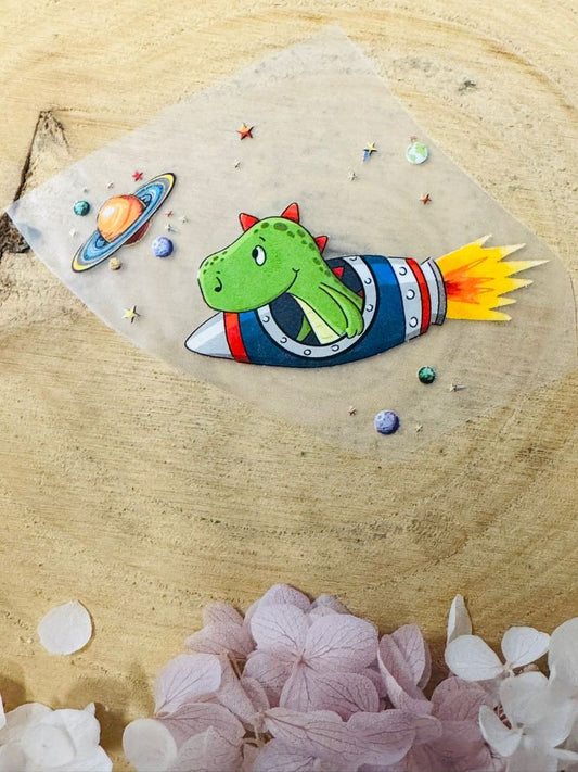 ein tolles Bügelbild aus der Growi Kollektion mit einem Dino in einer Rakete sitzend abgebildet