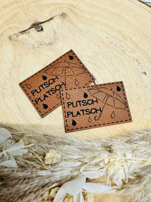 braunes  kunstlederlabel mit dem spruch plitsch platsch und einem regenschirm abgebildet