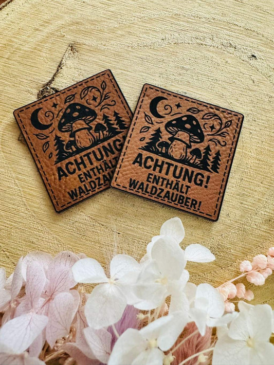 superweiches braunes Kunstlederlabel mit dem Spruch Achtung enthält Waldzauber und kleinen Waldpilzen abgebildet