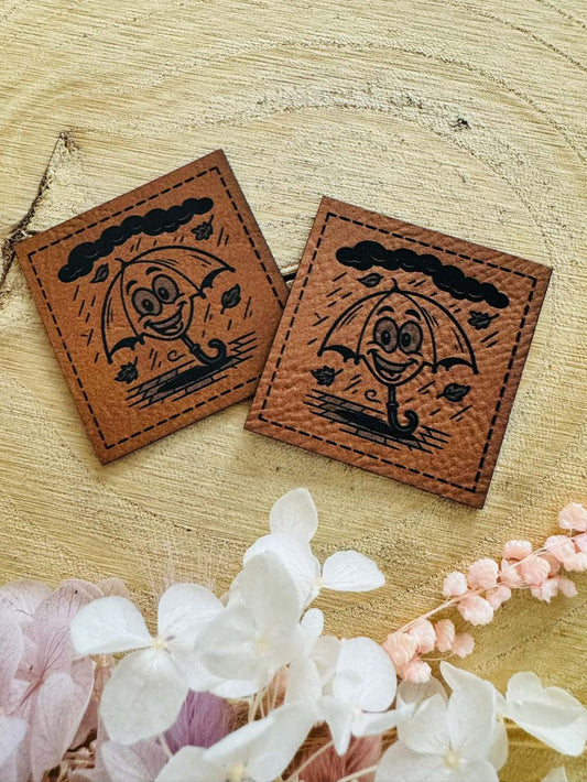 superweiches braunes Kunstlederlabel mit einem lachendem tanzenden Schirm im Regenwetter abgebildet 
