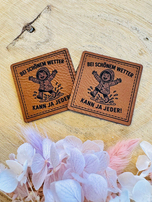 superweiches braunes Kunstleder Label mit dem Spruch Bei schönem Wetter kann ja Jeder und einem kleinen Kind tanzend in einer Regenpfütze
