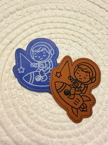 superweiches Kontur Kunstlederlabel mit einem kleinen Boy auf einer Rakete sitzend in Blau und Braun