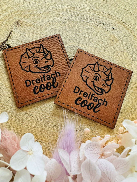 superweiches braunes Kunstleder Label mit dem Spruch Dreifach cool und einem lächelndem Dino abgebildet
