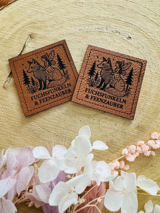 superweiches braunes Kunstlederlabel mit dem Spruch Fuchsfunkeln und Feenzauber mit einer kleinen Fee auf einem Fuchs in einem Wald sitzend abgebildet