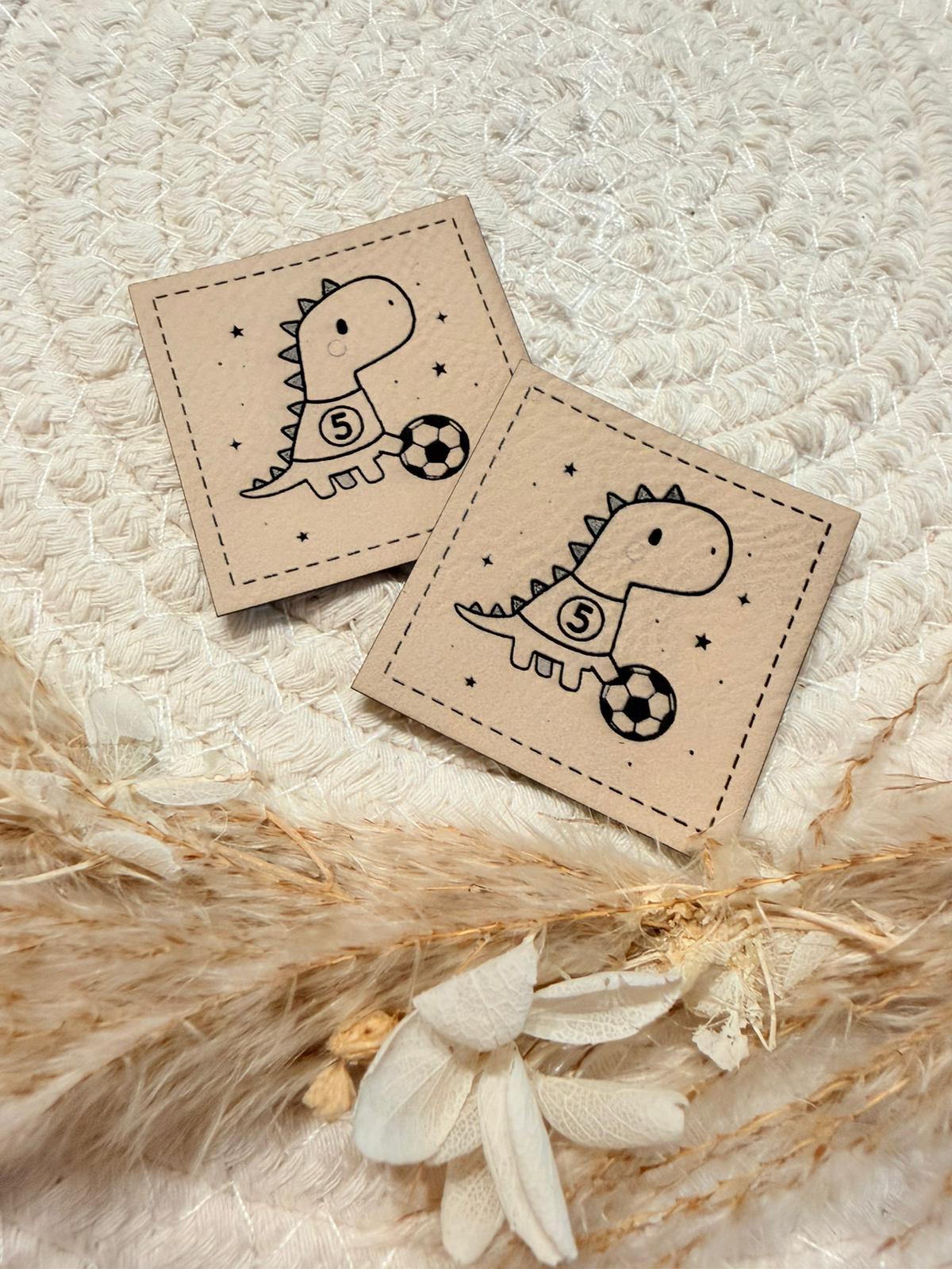 superweiches beiges Kunstlederlabel mit einem kleinen lustigen fussballspielenden Dino abgebildet
