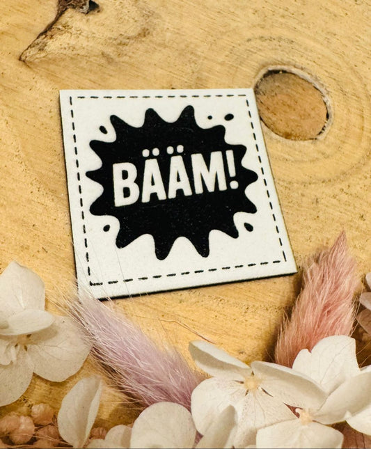 superweiches weisses Kunstlederlabel exclusiv von Bienenkinder, dass im Dunkeln leuchtet mit dem Spruch BÄÄM!