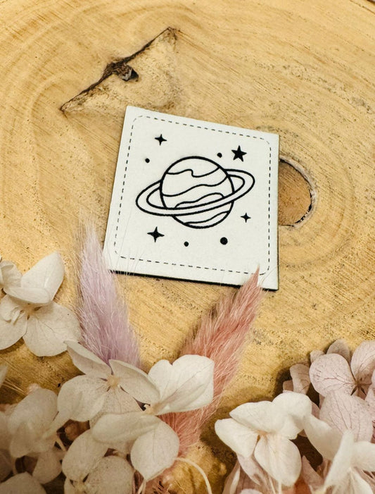 exclusives superweiches weisses Glow in the Dark Kunstleder Label, welches im Dunkeln leuchtet, mit einem Planeten im All abgebildet