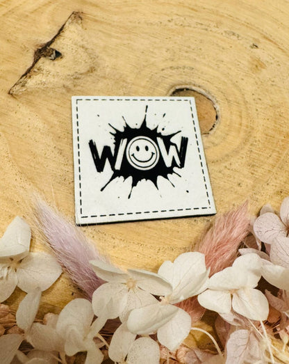 exclusives superweiches weisses Glow in the Dark Kunstleder Label der Bienenkinder, welches im Dunkeln leuchtet, mit einem Smiley und dem Spruch WOW abgebildet