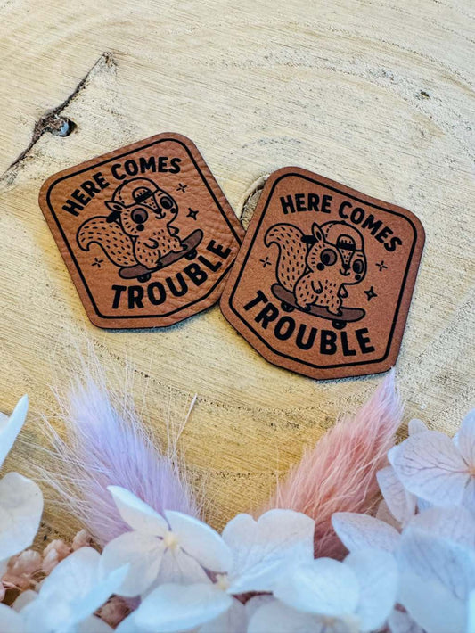 superweiches braunes Kunstleder Label mit einem kleinen skatenden Eichhörnchen abgebildet und dem Spruch Here comes Trouble