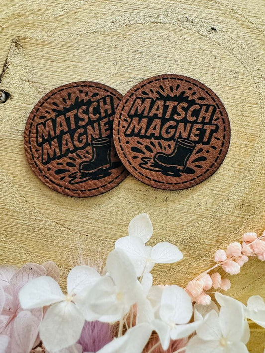 superweiches rundes braunes Kunstlederlabel mit dem Spruch Matsch Magnet und einem abgebildeten Stiefel in einer Pfütze