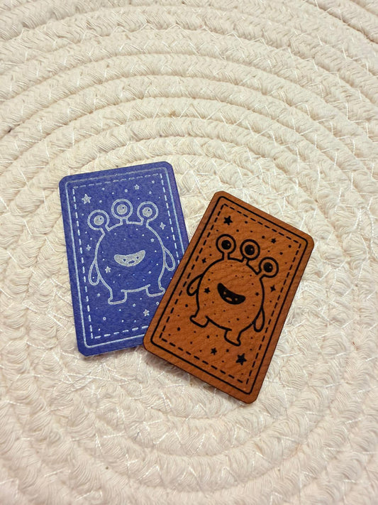 superweiches Kunstlederlabel mit einem dreiäugigen Monsterchen in blau und braun