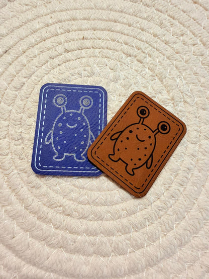 superweiches Kunstlederlabel mit einem kleinen zweiäugigen Monster in blau und braun