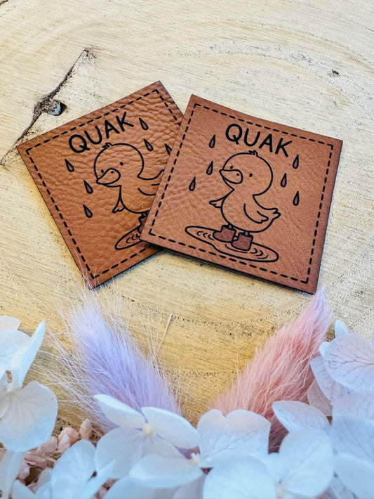 superweiches braunes Kunstleder Label mit einer kleinen Ente im Regen stehend und dem Spruch Quak abgebildet