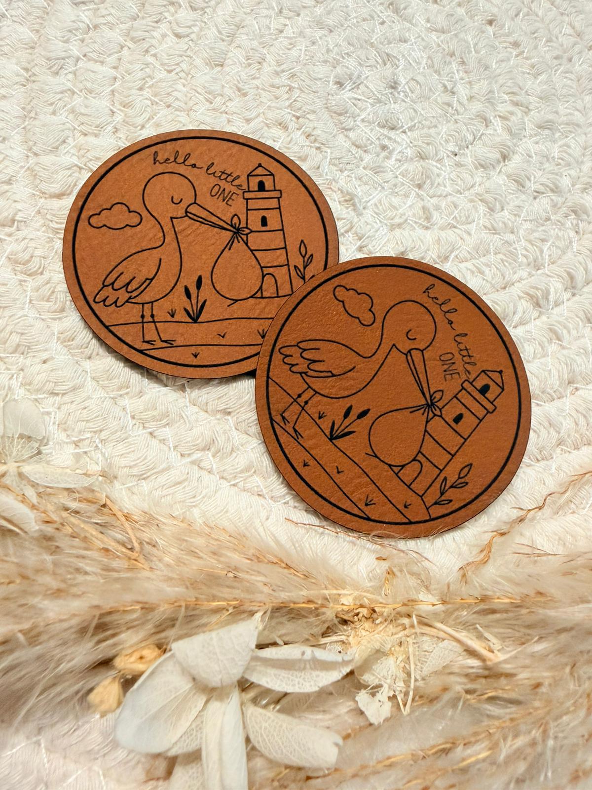 superweiches rundes braunes Kunstlederlabel mit dem Spruch Hello little One und einem niedlichen Klapperstorch abgebildet
