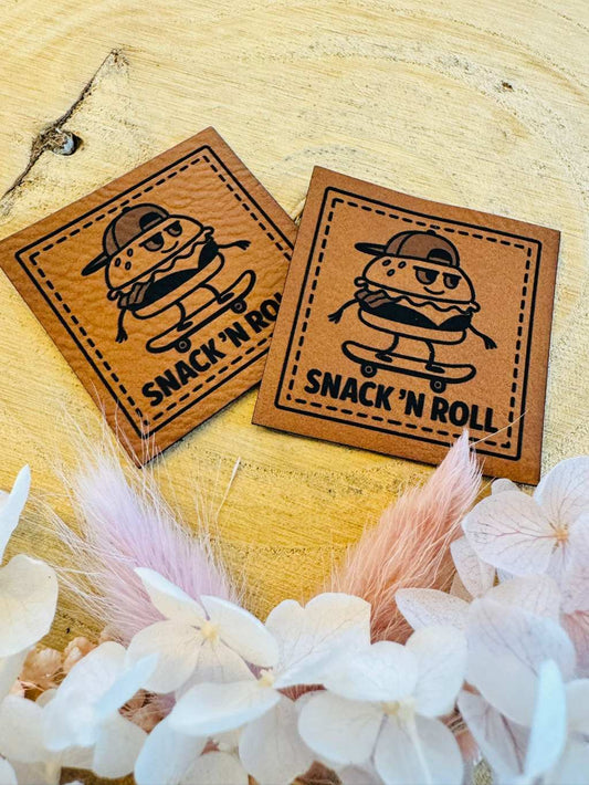 superweiches braunes Kunstleder Label mit dem Spruch SNACK`N ROLL und einem skatenden Hamburger abgebildet