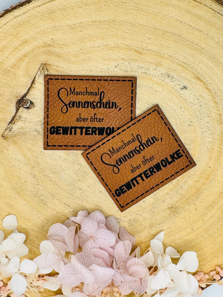 superweiches braunes Kunstlederlabel mit dem Spruch Manchmal Sonnenschein komma aber oefter Gewitterwolke