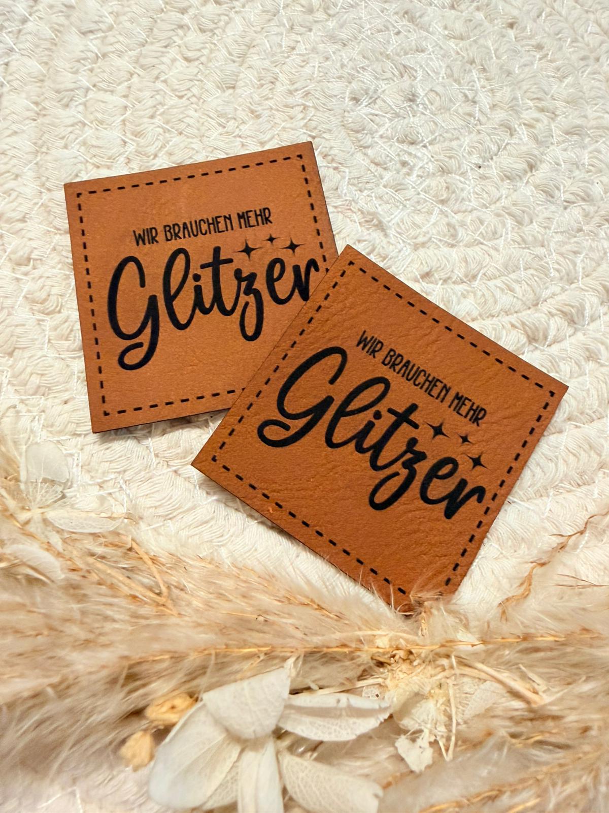 superweiches braunes Kunstlederlabel mit dem Spruch Wir brauchen mehr Glitzer