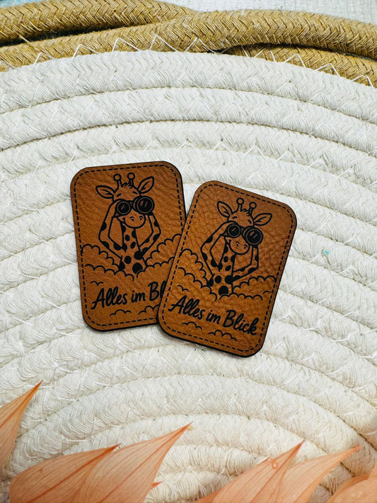 cooles neues superweiches Kunstlederlabel von den Bienenkindern mit dem Spruch Alles im Blick und einer coolen Giraffe mit Fernglas abgebildet
