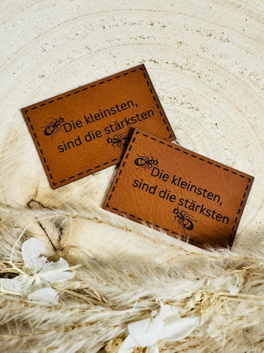 superweiches braunes Kunstlederlabel mit dem Spruch Die kleinsten sind die stärksten und kleinen Ameisen abgebildet