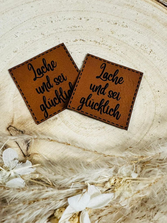 superweiches braunes Kunstlederlabel mit dem Spruch Lache und sei glücklich in schwarzer Schrift