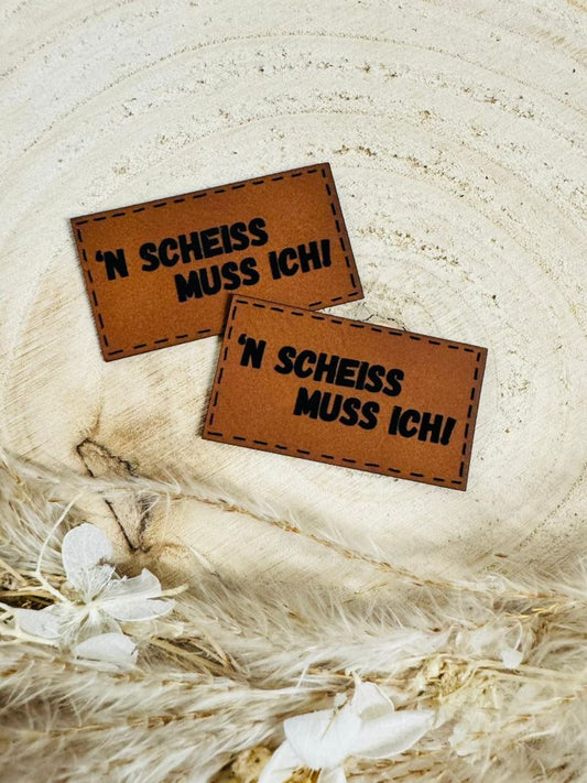 superweiches braunes Kunstlederlabel mit dem Spruch N`Scheiss muss ich Ausrufezeichen in schwarzen Buchstaben