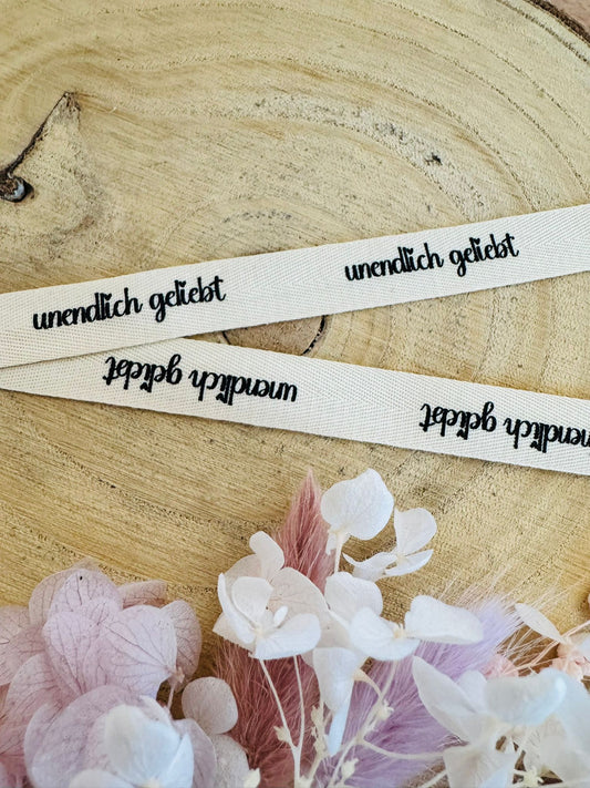 schönes weisses Baumwoll Webband mit dem durchgehenden Spruch unendlich geliebt in schwarzer Schrift