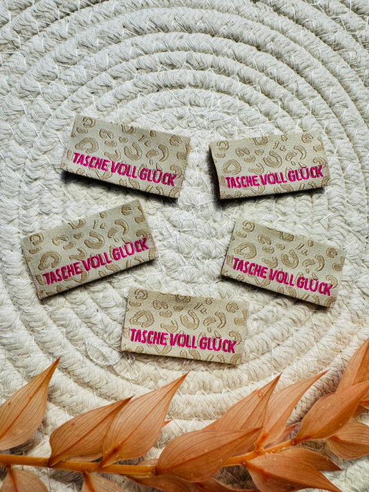 tolles Baumwoll Klapp Weblabel mit dem Spruch Tasche voll Glück auf beigem Leolook Untergrund